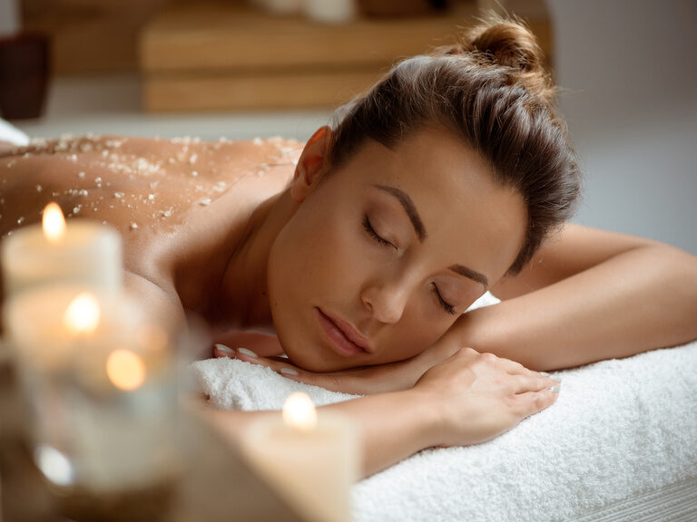 Eine Frau liegt entspannt auf einer Wellnessliege, umgeben von sanftem Kerzenlicht im Braunschweiger Hof.